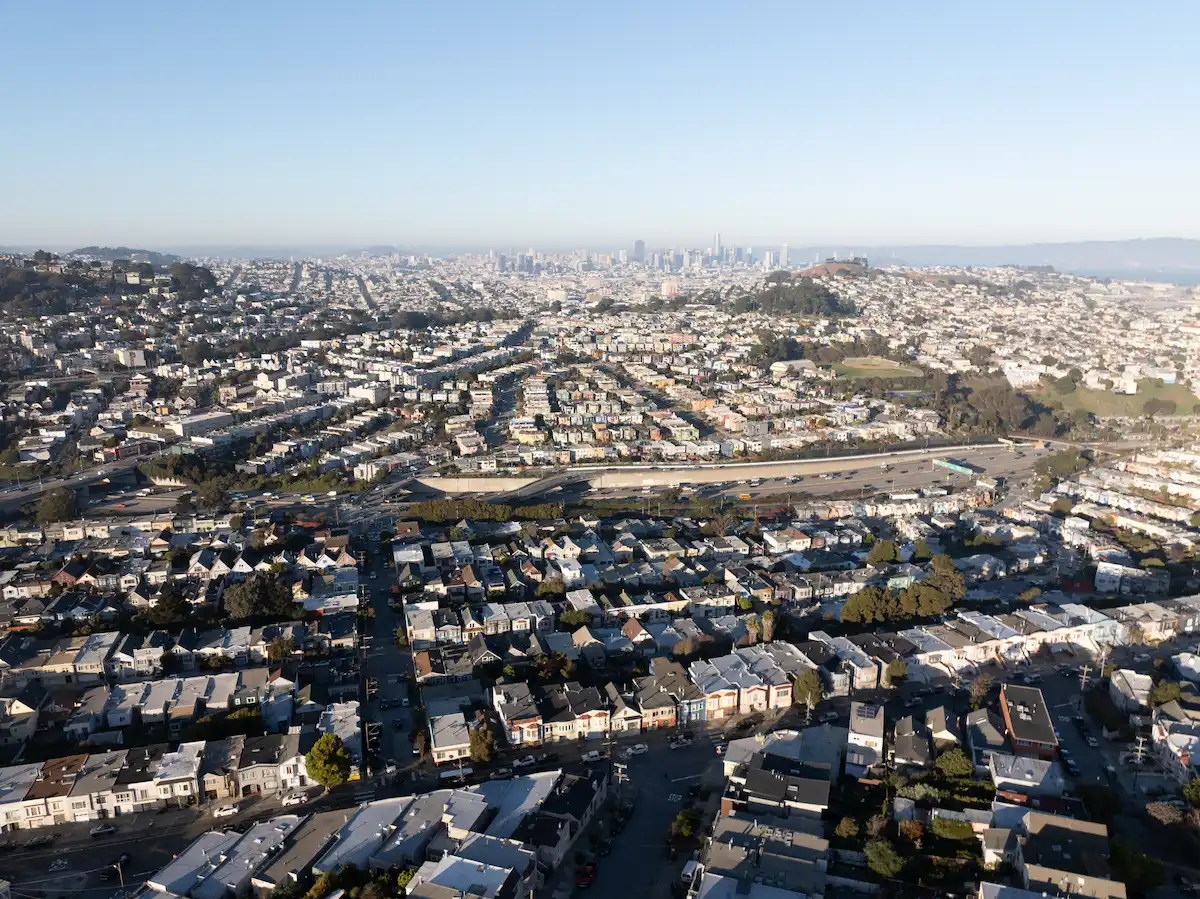 Aerial view of dense San Francisco Bay Area rooftops with the downtown skyline in the background.