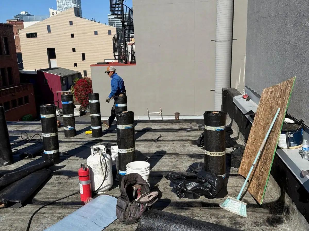 Roofing contractor working on a flat commercial roof with rolled underlayment material during a re-roofing project.