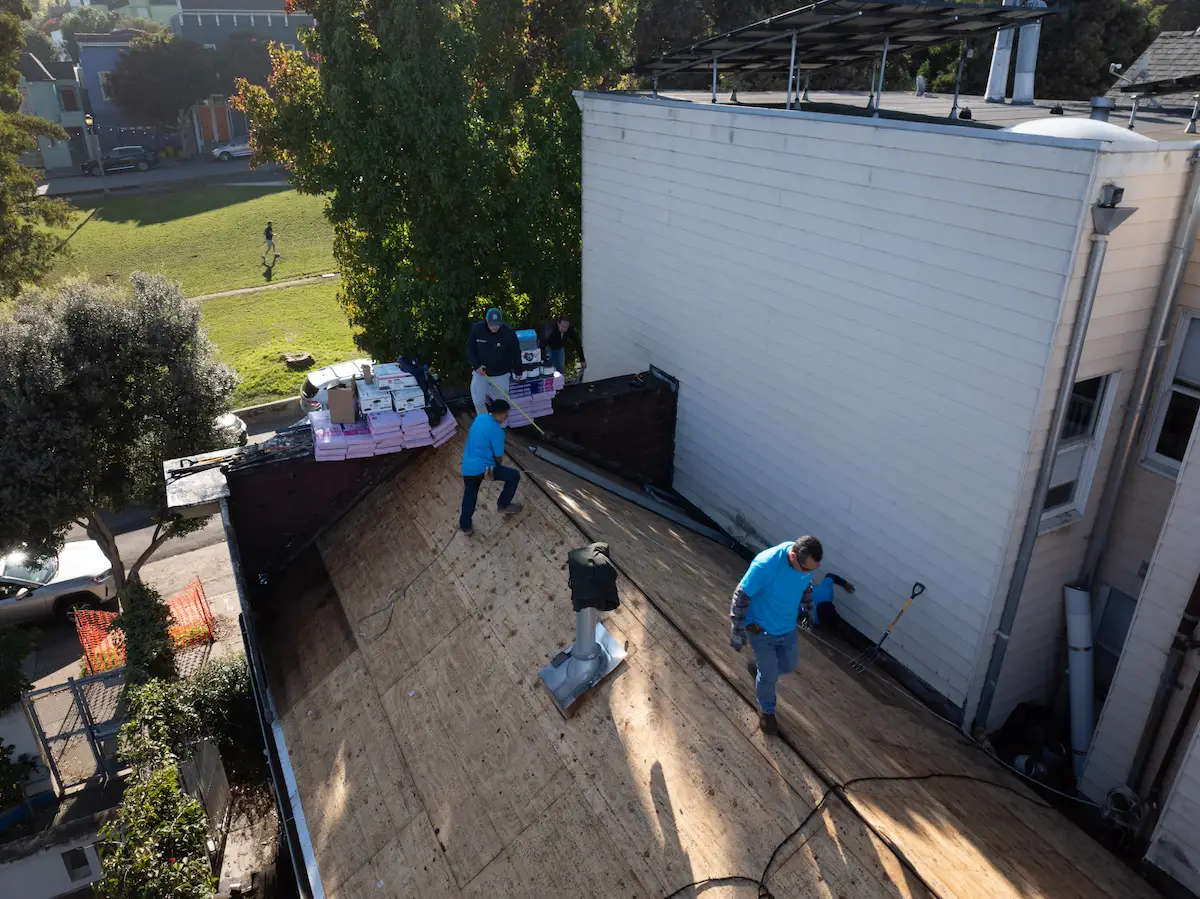 Roofing crew removing old shingles and preparing the plywood deck during a roof project on a San Francisco home.
