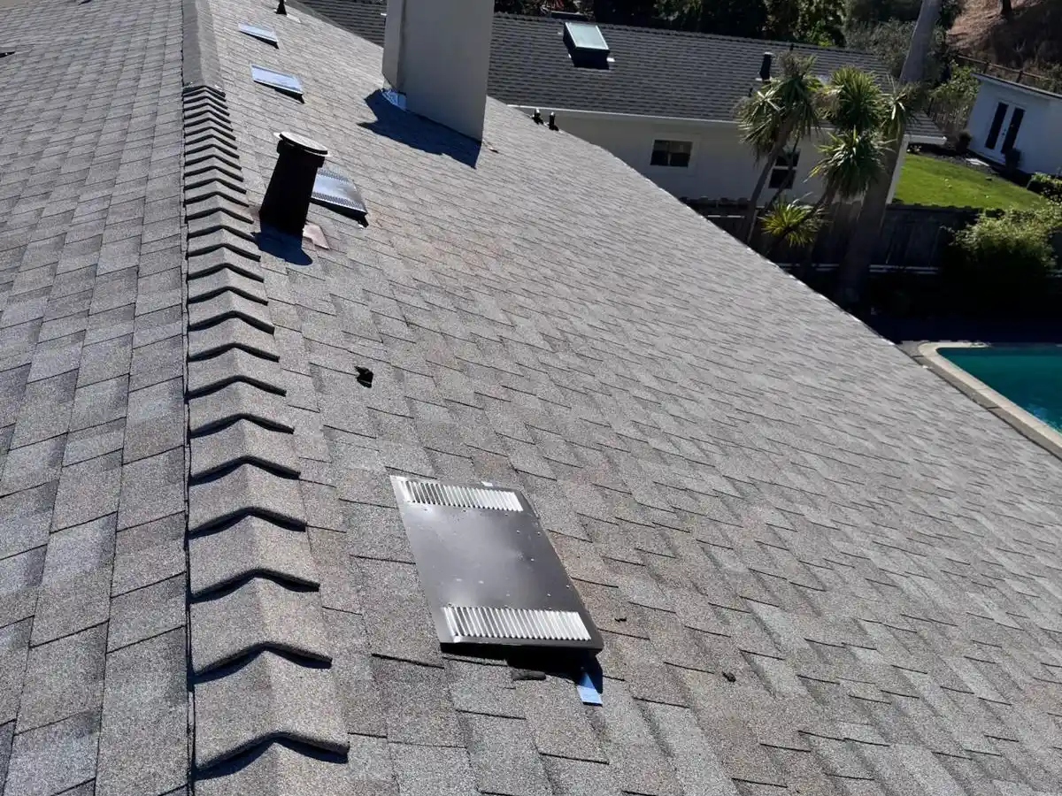 Aerial view of a shingle roof showing vent stacks, skylights, and chimney flashing — common inspection points for roof maintenance.