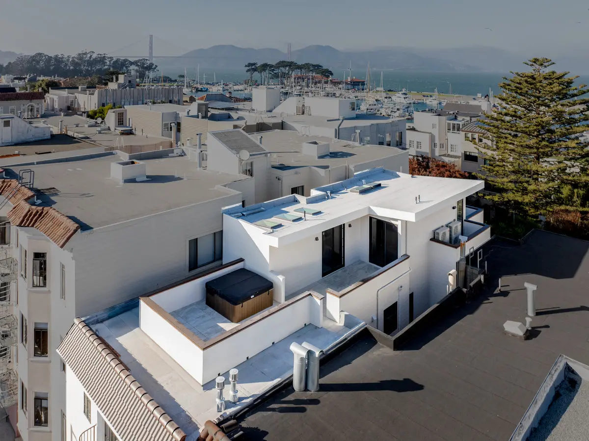Aerial photo of a flat membrane roof on a residential property in the San Francisco Bay Area with a marina and coastal hillside visible in the background, illustrating a completed flat roof system.