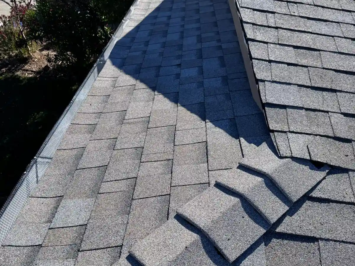 Close-up aerial view of asphalt shingles on a residential roof, showing shingle texture and lifted edges near a valley.