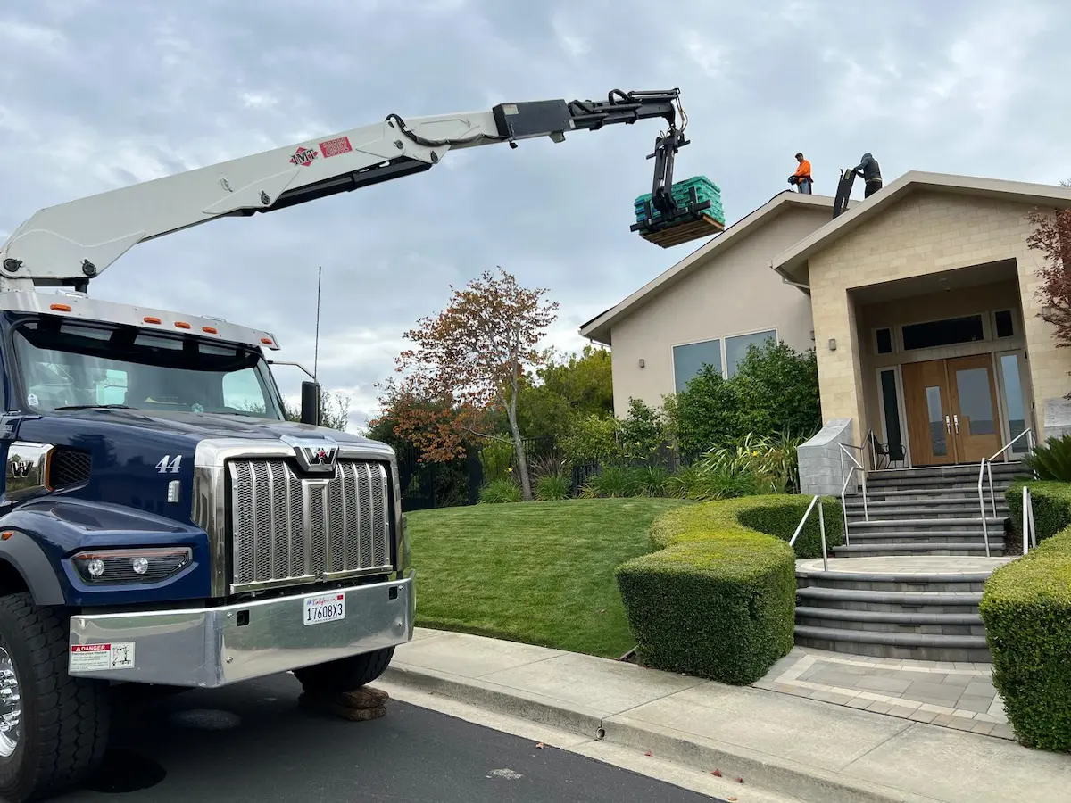 Crane truck delivering bundles of roofing material to a residential job site for a roof replacement project.