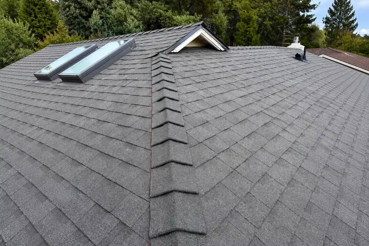 Aerial view of a completed asphalt shingle roof with skylights, ridge cap detailing, and clean valley flashing on a residential home.