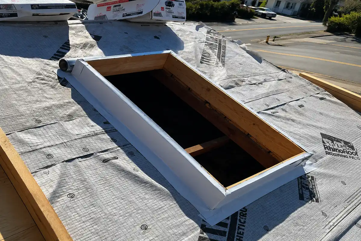 Close-up of a skylight curb framed and wrapped with synthetic roofing underlayment during a roof replacement project.