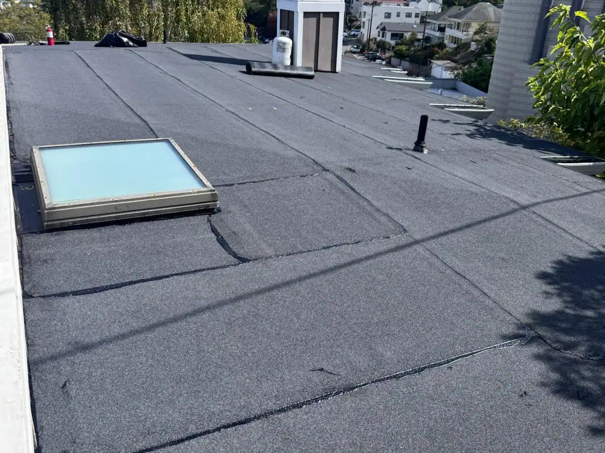 Aging flat roof membrane with visible seam wear, patch repairs, and an older skylight showing signs it may need replacement.