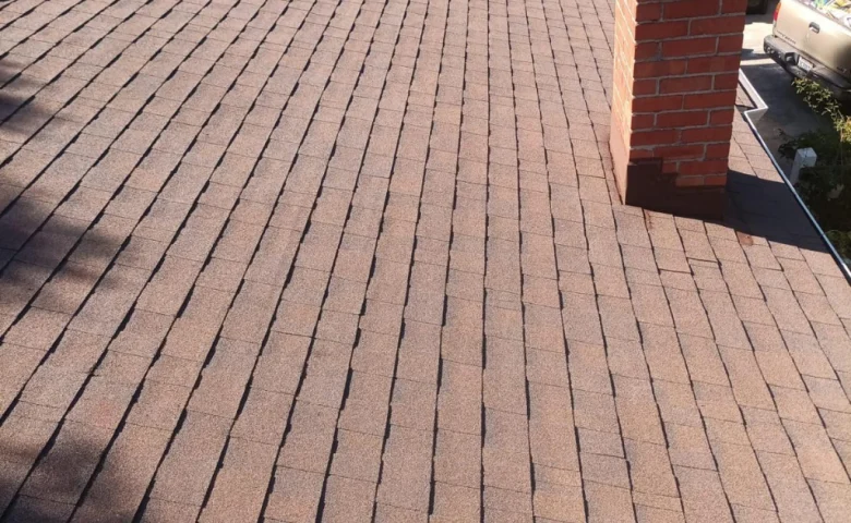 Viewed from above, a roof in San Francisco showcases brown asphalt shingles with a red brick chimney.